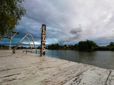 Low angle view if an empty wooden boardwalk or deck overlooking a calm lake under a cloudy sky