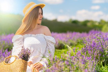 Elegant young woman in an off the shoulder white dress and straw sunhat posing in a field of summer lavender