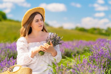 Pretty young woman posing with fresh lavender in a field in a trendy summer outfit enjoying the sunshine