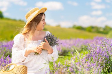 Young woman posing amongst purple lavender bushes in summer holding a bunch of fresh flowers in her arms