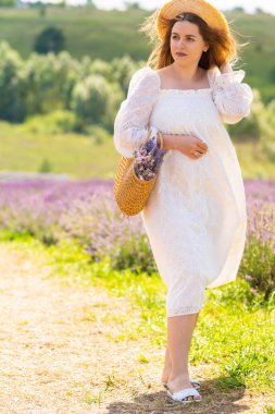 Thoughtful young woman strolling through lavender fields wearing a white summer dress and sunhat