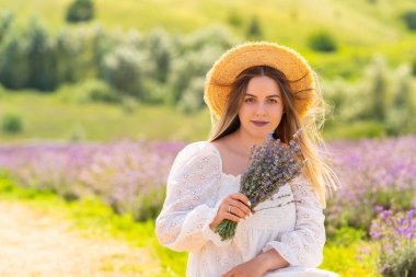 Quiet serious young woman holding a bunch of lavender she has just picked in the field with copyspace