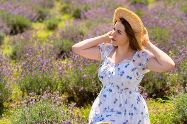 Attractive young woman posing in a straw sunhat in summer against a backdrop of lavender in a farm field