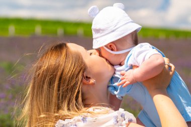 Tender portrait of a young mother kissing her baby as she holds him aloft outdoors in a field of lavender in summer