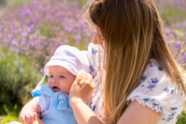 Caring young mother adjusting the sunhat on her baby outdoors on a summer day in a field of lavender