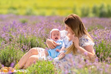 Young mother playing with her happy baby son as they relax together on a hot summer day in a field of lavender