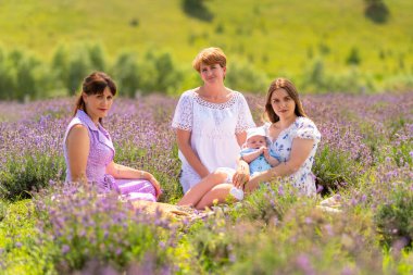 Three women sitting amongst lavender with a small baby boy in lush green countryside all looking at the camera