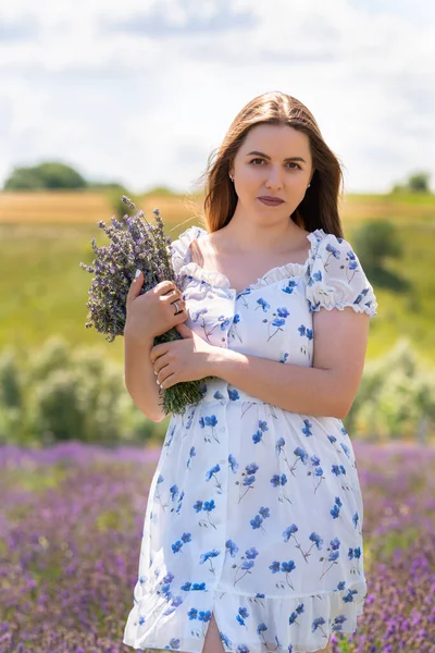Young woman walking through lavender field with bunch of flowers clasped in her arms as she approaches the camera