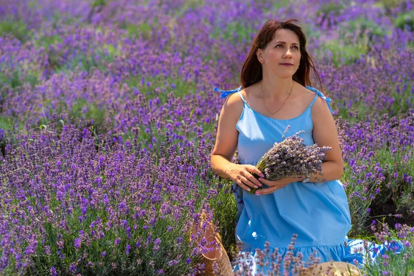 Pretty woman sitting in a field of lavender in summer holding a bunch of flowers and looking up with a quiet smile of contentment