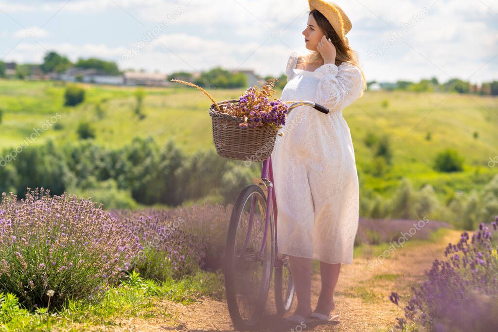 Young woman walking through lavender fields wheeling a bicycle on a warm summer day looking off to the side