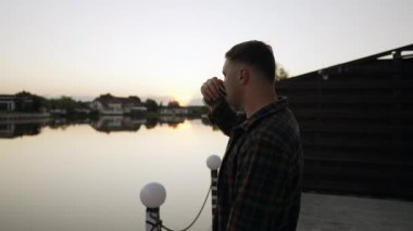 Gün batımının tadını çıkarırken bir fincan kahveyi yudumlayan bir adam yansımalarıyla sakin bir gölün üzerinde.