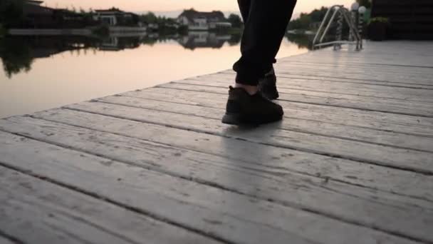 夕阳西下 在宁静的湖面上 一个人在木制甲板上行走 他的脚步声的角度很低 — 图库视频影像