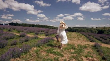 Elegant young woman walking away through lavender fields in a fresh white cotton dress and straw sunhat in summer