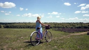 Country woman wheeling her bicycle through hills in a lush green landscape in evening light viewed from the side