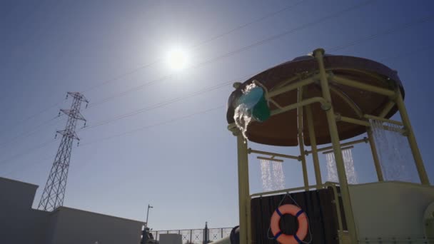 澄んだ青い空の明るい夏の太陽に照らされた休日のリゾートでのウォータースライドの屋根からの水のカスケード — ストック動画