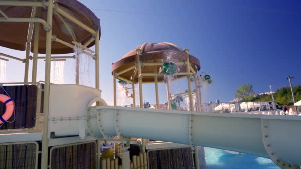 ウォータースライダーの開始時に遊園地内の上昇した水の機能を水でカスケードオフ旅行や観光のコンセプトで下に輝くプール — ストック動画
