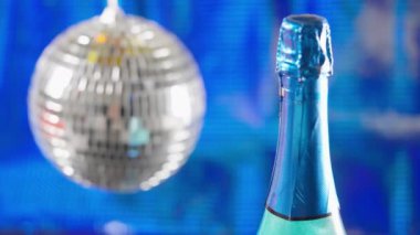 Christmas bauble and bottle of champagne for the holiday season in close up over a blue background with focus to the sparkling wine