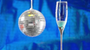 Pouring blue champagne into an elegant flute or glass with metallic silver party decoration or bauble in a concept of Christmas, New Year, valentines or a Special Occasion