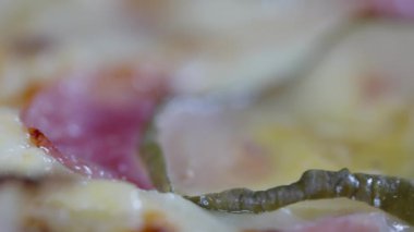 Close upon the ingredients of a freshly baked Italian pizza with melted mozzarella cheese, ham and gherkin pickle in a full frame view