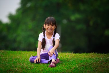 Yeşil çimenlerin üzerinde oturan genç kız gülümseyerek