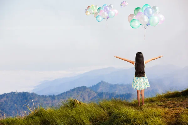 Little girl standing at high mountain and looking balloon in the — Stock Photo, Image