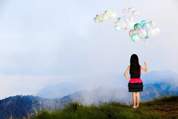 Niña de pie en la alta montaña y mirando globo en el —  Fotos de Stock