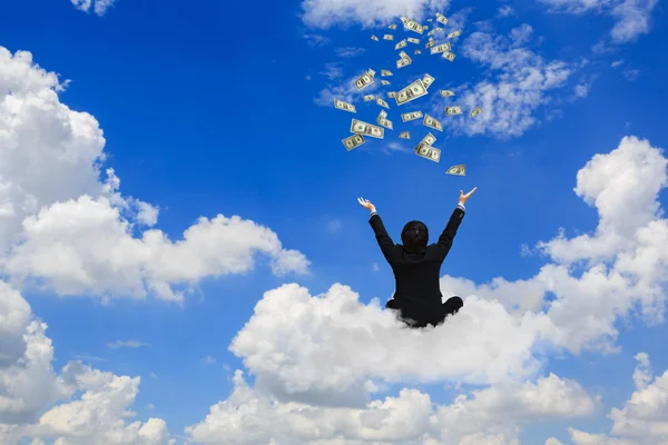 Young businessman sitting on the cloud with a lot of falling dol — Stock Photo, Image