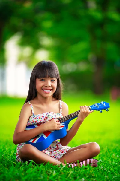 Aziatische meisje, zittend op het gras en play ukulele — Stockfoto