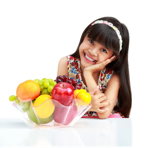 Счастливая маленькая азиатская девочка сидит на столе с тарелкой фруктов — стоковое фото