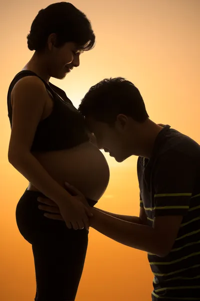 Asian father kissing her pregnant wife's tummy at sunset — Stock Photo, Image