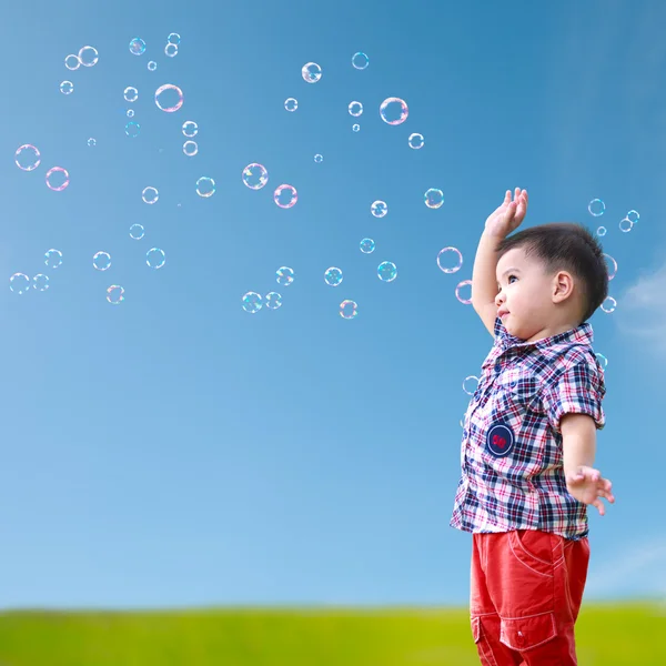 Bebê pouco asiático menino de pé contra azul céu com sabão bolha — Fotografia de Stock