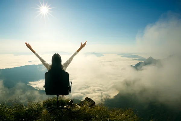 Young woman sits on a chair and open her arms at the top of the — Stock Photo, Image