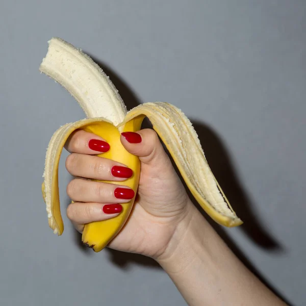 Hand met rode nagels houdt een banaan — Stockfoto