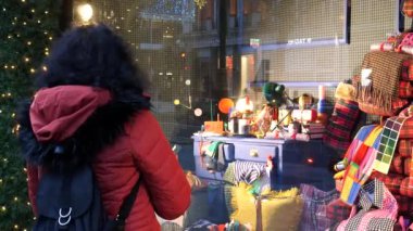 Sırt çantalı kırmızı ceketli turist kadın mağazanın önünde Noel ağacının yanında duruyor ve hediye seçimine bakıyor..