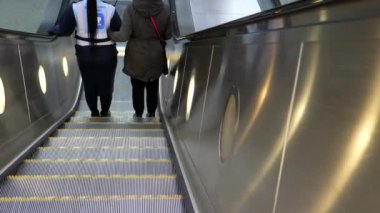 Metro ya da metro istasyonunda yürüyen merdivenle inen kimliği belirsiz iki kadının arka görüntüsü. Bastonlu kör kadın yürüyen merdivenin sonuna yaklaşırken görüş rehberine tutunuyor..