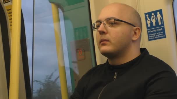 坐在移动中的地铁车厢或地铁车厢的优先座位上戴眼镜的年轻人 — 图库视频影像