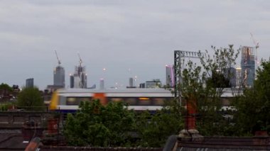 Tren, Londra 'nın yukarısındaki konut çatılarında, gökdelenler ve arka planda inşaat vinçleri ile hareket ediyor..