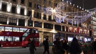 LONDON, UNITED KINGDOM - CIRCA NOVEMBER, 2020: Covid-19 salgını sırasında Noel zamanı, Regent Caddesi 'nin yukarısında aydınlanmış melek figürü, ünlü dükkanların önünden geçen turistler, bazı insanlar maske takıyor.