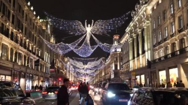 LONDON, UNITED KINGDOM - CIRCA NOVEMBER, 2020: Geceleyin Regent Caddesi 'nin ortasında aydınlanmış Noel melekleri altında fotoğraf çeken turistler, siyah taksiler yavaşça geçip gidiyorlar.