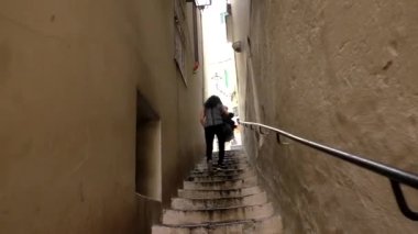 Yetişkin bir turist kadının Amalfi kıyısındaki evler arasındaki dar geçitte uzun ve sarp adımlarla tırmanmasını izleyen el kamerası..