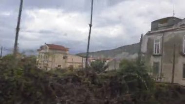 Moving train passenger window view of gardens and buildings in rural Italy.