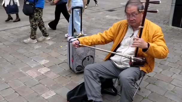 2021年9月9日 Circa September 英国英格兰曼彻斯特 在市中心行人区 人们走过中国老年人身边 演奏传统的双弦弓形乐器二胡 — 图库视频影像