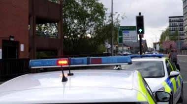 Büyük Manchester 'daki Stockport kasabasının caddesinde park etmiş iki polis arabasının üstünde kırmızı ışıklar yanıp sönüyor. Seçici bir odak noktası var..