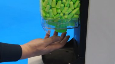 Erkek el, kulak tıkacı makinesinden mavi arka planda dönerek kulak tıkacı alıyor..