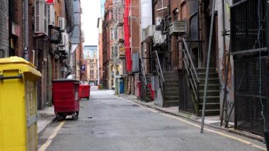 Manchester şehir merkezindeki çöp bidonları görünüyor. Arka planda kimliği belirsiz insanlar yürüyor..