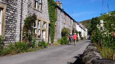 Millers Dale, Peak District Ulusal Parkı, İngiltere 'de küçük pitoresk bir köyde yürüyen iki olgun yürüyüşçünün arka görüntüsü.