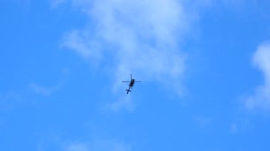 Mavi gökyüzünde, beyaz bulutların altında uçan polis helikopterinin alt görüntüsü..