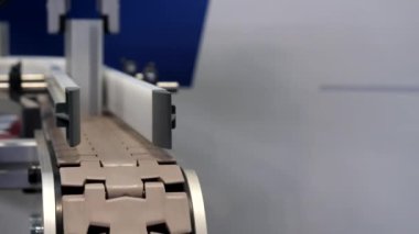 Advanced automated manufacturing system. Machine, robot hand placing production parts on moving plastic conveyor belt; selective focus on foreground, copy space.