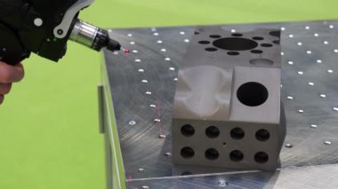 Hand holding laser scanner scanning intricate 3D metallic part.