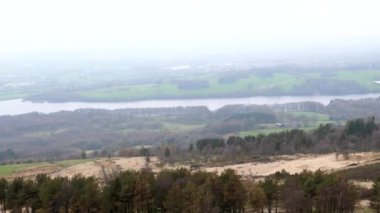 High angle panoramic view of Rivington reservoir from popular Winter Hill on a misty spring day; distant people, panning shot.